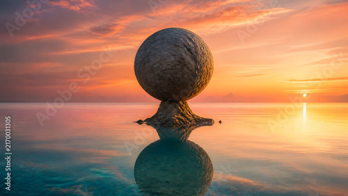 round boulder balanced on rock stack floating in calm water under warm glowing sunset sky
