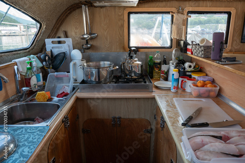 Fotografía Compact catamaran galley contains cookware, utensils and fresh cut fish prepared on counter during sea trip