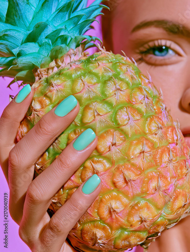 Turquoise nails wrapped around a golden green pineapple in close view. Ideal for beauty campaigns, tropical advertising, and pop art product branding.