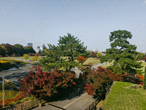 Kanazawa, Japan - 24 August 2026: View of Kenrokuen Garden with manicured lawns, vibrant autumn foliage, pine trees, and a walking path with a distant cityscape under a clear sky.