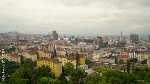 Vienna cityscape with colorful residential buildings, church spires, and modern skyscrapers under cloudy sky. Aerial view of Austrian capital's diverse architecture.