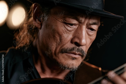 Close-up of mature man playing guitar with stage lights blurred