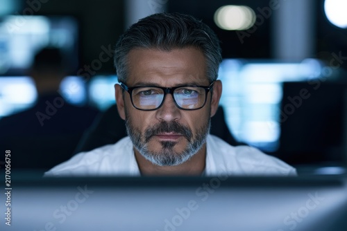 Middle-aged man wearing glasses concentrating on computer screen indoors