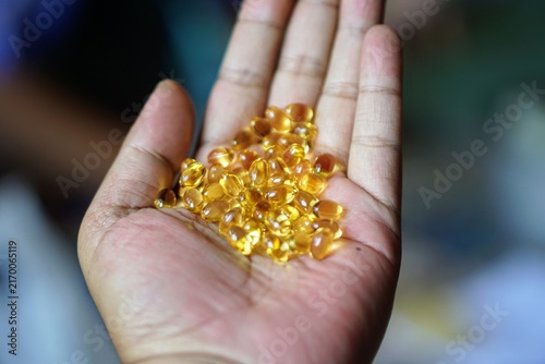 Close-up of a human hand holding a pile of golden yellow softgel fish oil capsules.