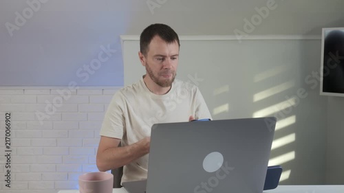 man celebrating success in modern office or home workspace with excited and productive mood, wearing white shirt and headphones, working on laptop, front view, business productivity.