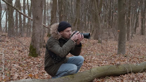 man photographing fallen leaves in the forest with a focused and concentrated side view of wooden trees and dry nature in brown and green tones, outdoor activities.