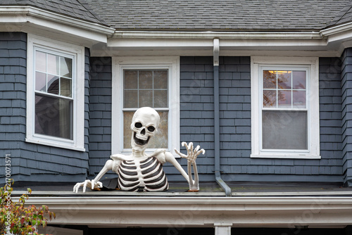 Cuadro en lienzo Halloween skeleton decoration emerging from porch roof of gray-blue suburban hou