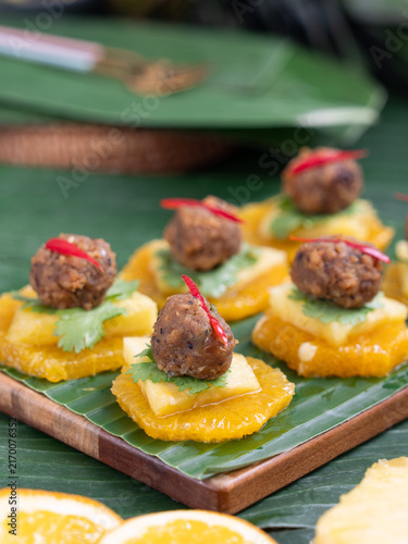 Traditional Thai appetizer Ma Hor with savory minced pork paste over fresh orange and pineapple slices served on banana leaf.