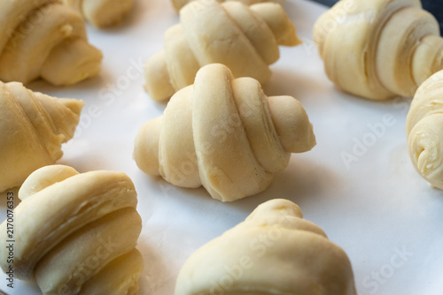 Close up of unbaked croissant dough shaped and proofed with several fluffy leavened ready for baking in the oven on a tray.