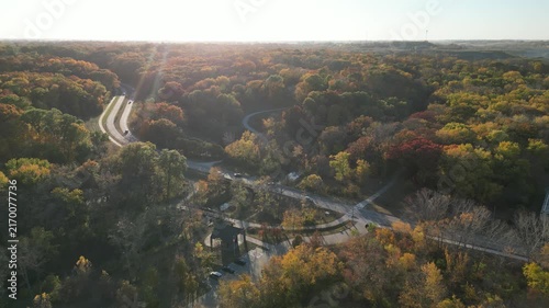 A divided road that winds into the trees and up the hill on a bright fall afternoon in the Midwest. 4k, drone, flying