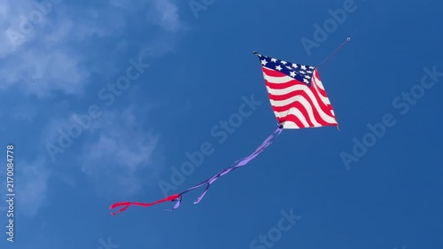 Patriotic American flag kite soars high against a vivid blue summer sky with wispy clouds, symbolizing freedom, recreation and American pride. 15327  