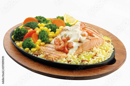 Foto Grilled salmon fillet topped with shrimp and white sauce, served with rice and steamed broccoli, corn, and carrots on a sizzler plate isolated on white