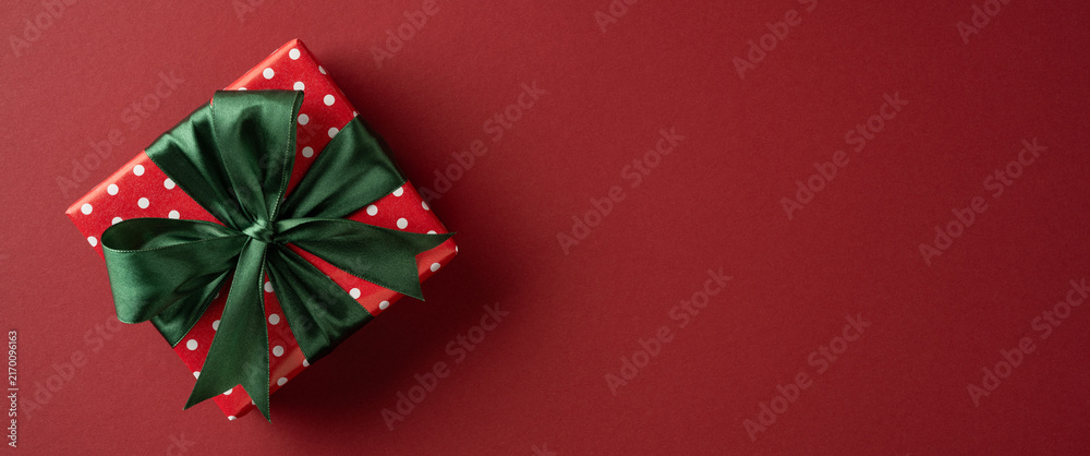 Fototapeta premium Red polka dot present with green satin bow for Merry Christmas and Happy New Year celebration ob banner maroon backdrop