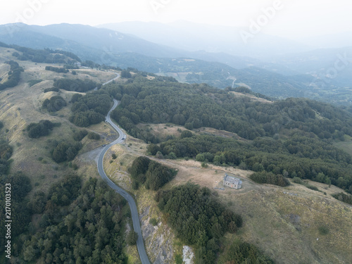 Aerial view of Parco Nazionale dell'Appennino Tosco-Emiliano featuring a winding mountain road, dense forests, and a solitary stone building in Provincia di Massa e Carrara, Italy.