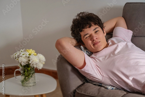 Obraz na plátne Teenage boy with an ironic smile resting on a sofa at home