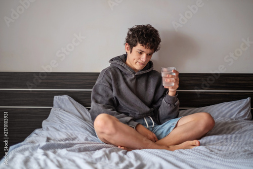 Fotografie Teenage boy with a glass of water in bed feeling better