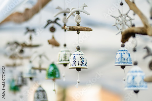 Handmade ceramic bells with decorative patterns hanging at an outdoor craft market. Artisan ornaments combine pottery, natural materials and traditional handmade design.