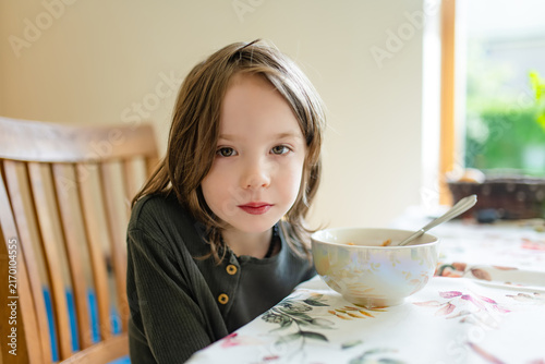 Obraz na plátně Young child sitting at a dining table and looking reluctant to eat his meal