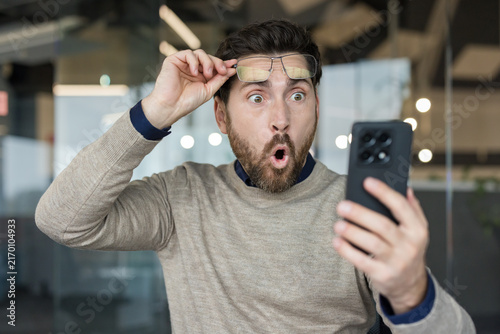 Fotografie Man with glasses pushed up on his forehead, looking at a smartphone with a wide-