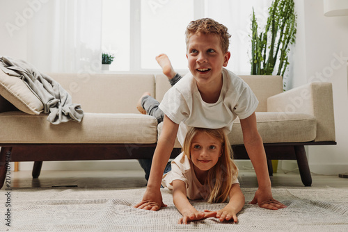 Fotografía Happy siblings playing together on carpet in cozy living room
