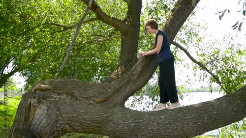 Happy child climbed on the trees. The girl is sitting on a tree branch. Little kid is playing in the park.