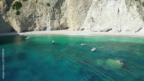 Aerial reverse shot showing turquoise sea and white cliffs at Chomi Beach in Corfu near Paleokastritsa with a boat passing by