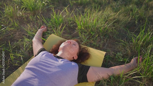 A woman rests peacefully on a yellow mat in the park. The park is filled with tall grass, creating a serene atmosphere for outdoor sport and relaxation.