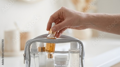 Hand taking glass serum bottle from transparent cosmetic bag at home