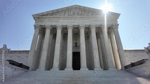 Tilt up establishing shot of the United States Supreme Court Building with its grand marble columns and steps under a bright blue sky in Washington, DC. 15336  