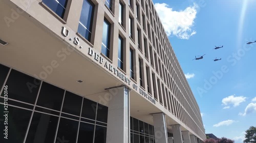 Tilt up view of the U.S. Department of Education headquarters in Washington, DC, as a formation of military helicopters flies across the blue sky. 15339  