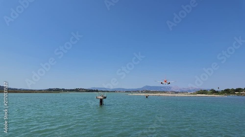 4K shot showing easyJet plane flying low over the causeway near the Greek Orthodox church at Corfu Airport with a female waving