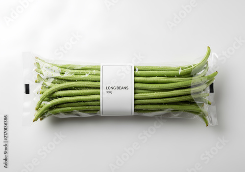 Fresh green long beans in a transparent plastic package with a white label, isolated on a white background.