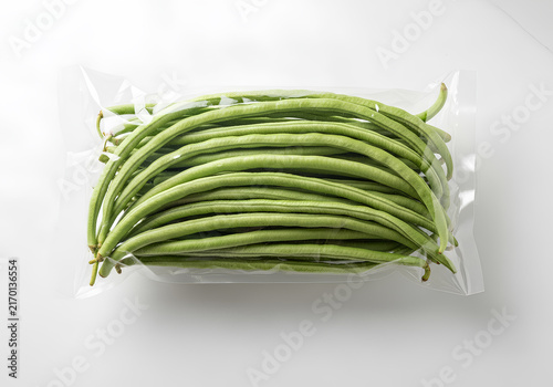 Fresh green long beans (Kacang Panjang) packed in a clear plastic bag on a white background. Top view of raw yardlong beans for cooking.