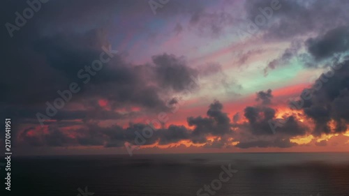 Dark storm clouds and vivid sunset colors create a striking evening sky above the calm Atlantic Ocean.