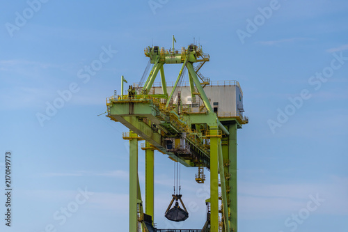 Fotografie Low angle shot of a massive green industrial harbor crane machine lifting a heav