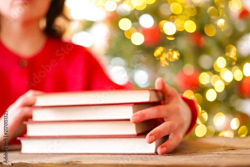 Holiday Reading and Learning with Books at Christmas.Woman Reading Books During Christmas Winter Holidays.hardcover books beside a glowing Christmas tree for bookstore advertising, library events