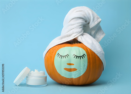 Creative pumpkin decorated with face mask design wrapped in towel with skincare product