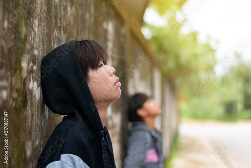 Depressed and lonely teenage boy in a black hoodie leaning against an old wall, feeling anxious and isolated from family or generation gap.