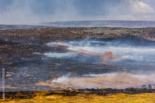 Smoke rising from burnt ground after wildfire on Llangynidr Moors, Brecon Beacons, charred earth and scorched vegetation across upland landscape