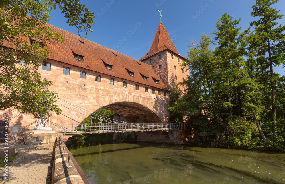 Fototapeta premium Historic stone gate with a tower beside the Pegnitz River on a sunny summer day in Nuremberg, Germany.
