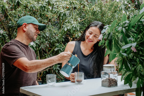 Konstfotografi Couple sharing a relaxed coffee moment outdoors as a man pours freshly brewed coffee for a smiling woman surrounded by lush vegetation