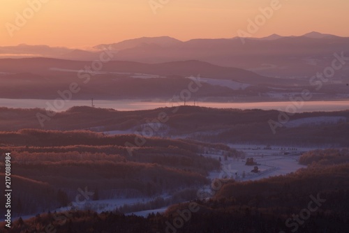 Obraz na plátne Mountain range hazy in the sunrise glow over snowy farmland, Hokkaido, Japan