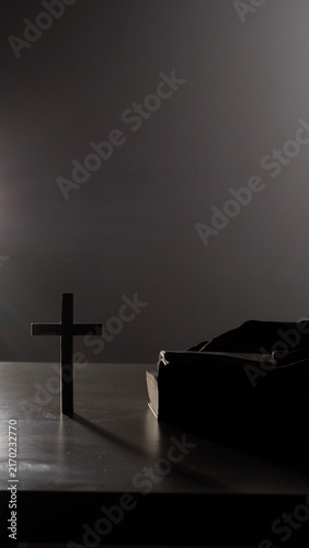 Fotografía Wooden cross standing beside a holy bible, both partially silhouetted on a dark