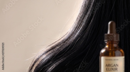 Smooth black hair flowing background with a dropper bottle of argan oil elixir for natural hair care treatment