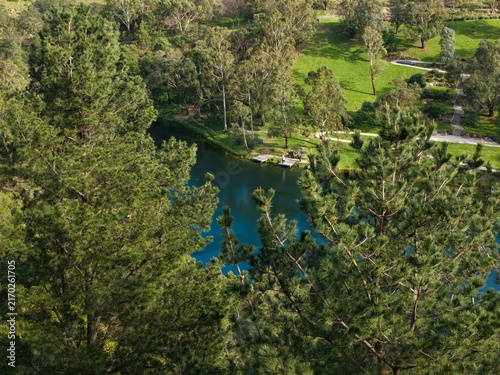 Ferntree Gully, Victoria, Australia - 11 July 2026: Aerial view of Ferntree Gully Quarry Recreation Reserve featuring a deep blue lake, surrounding trees, and people on a wooden dock.