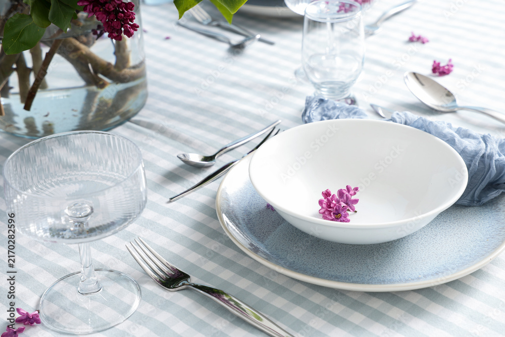 Naklejka premium Spring dining table setting with lilac flowers, elegant dinnerware, and striped tablecloth for special occasions