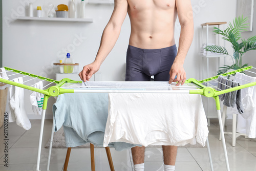 Young man in underpants hanging clean clothes on dryer at home
