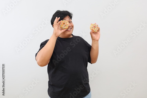 Quadro su tela An overweight Asian man stands against a plain white background, posing while holding two doughnuts