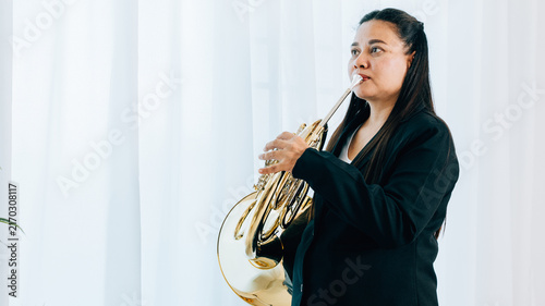 Fotografie Dressed in black, a woman blows a gleaming French horn in gold