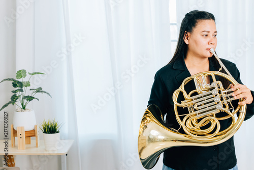 Canvas Print Dressed in black, a woman blows a gleaming French horn in gold